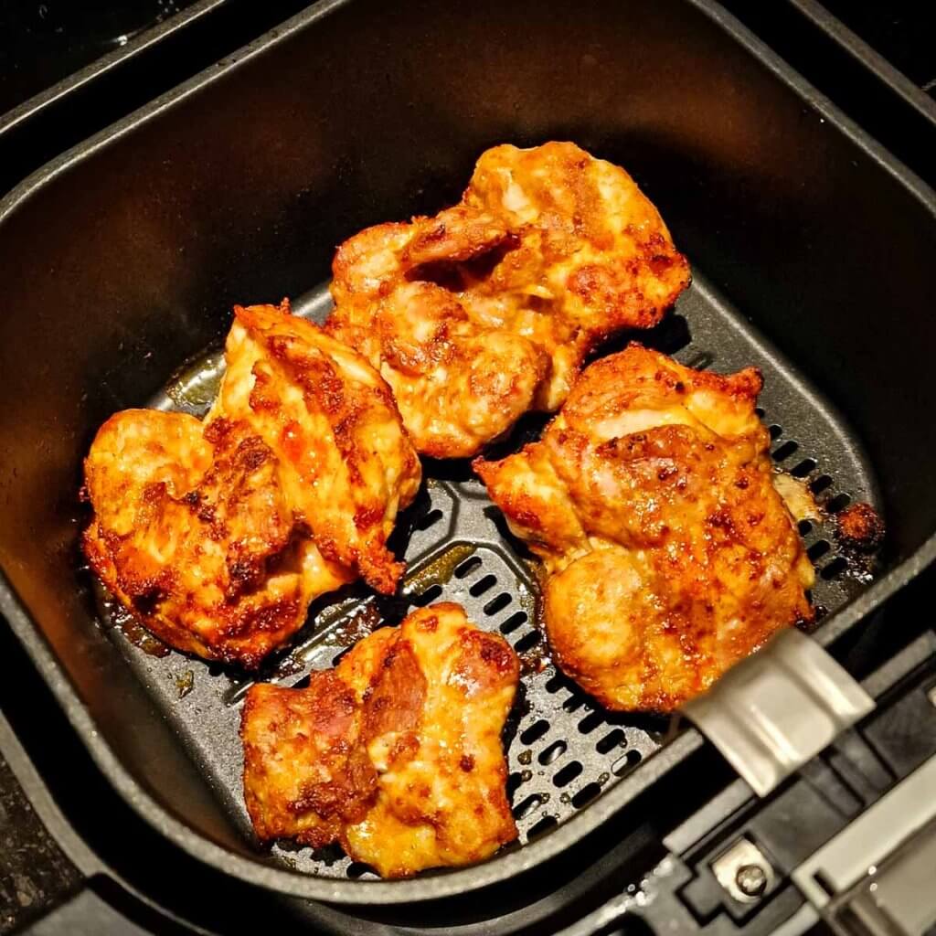 Air fried boneless chicken thighs in air fryer basket.