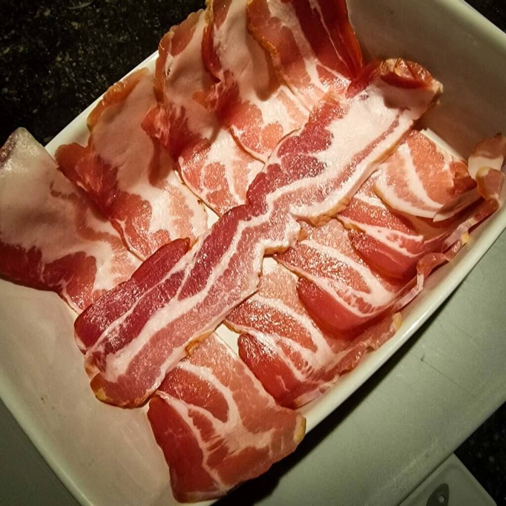 raw bacon strips in an oven tray.