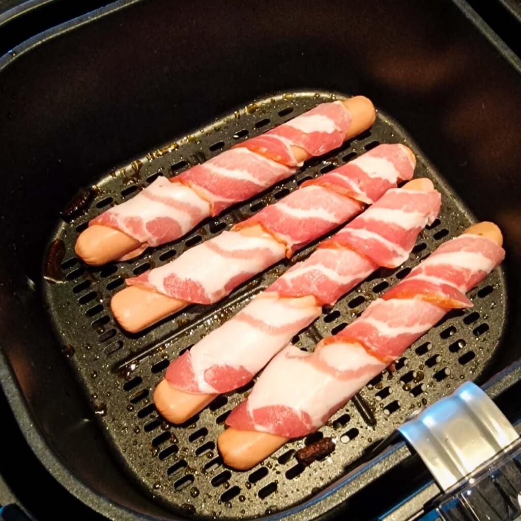 raw bacon-wrapped hot dogs in the air fryer basket.