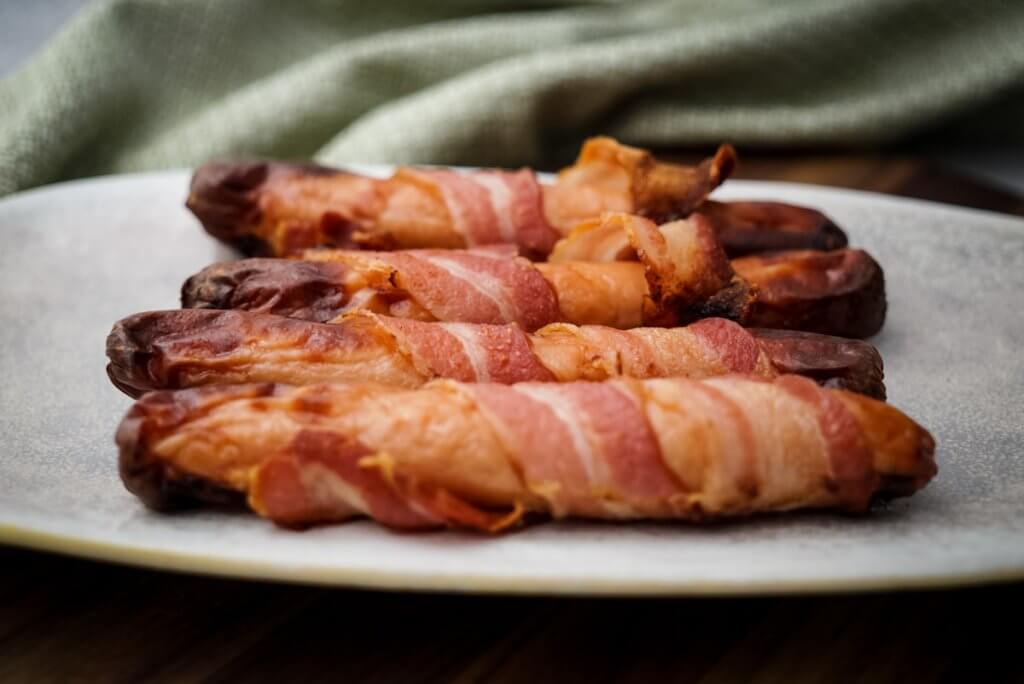 bacon-wrapped hot dogs served on a plate.