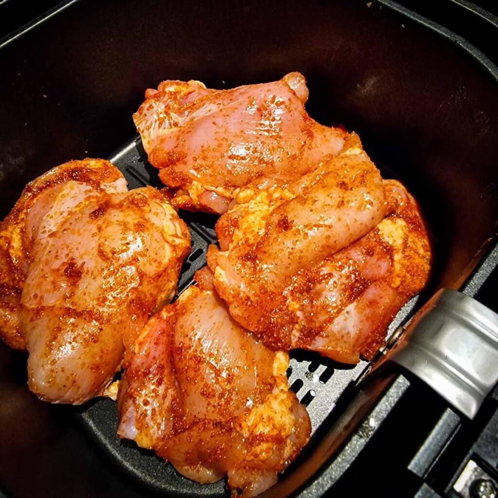 Raw boneless chicken thighs in air fryer basket